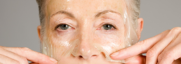 Frau zieht transparente Maske nach chemisches Peeling vom Gesicht ab